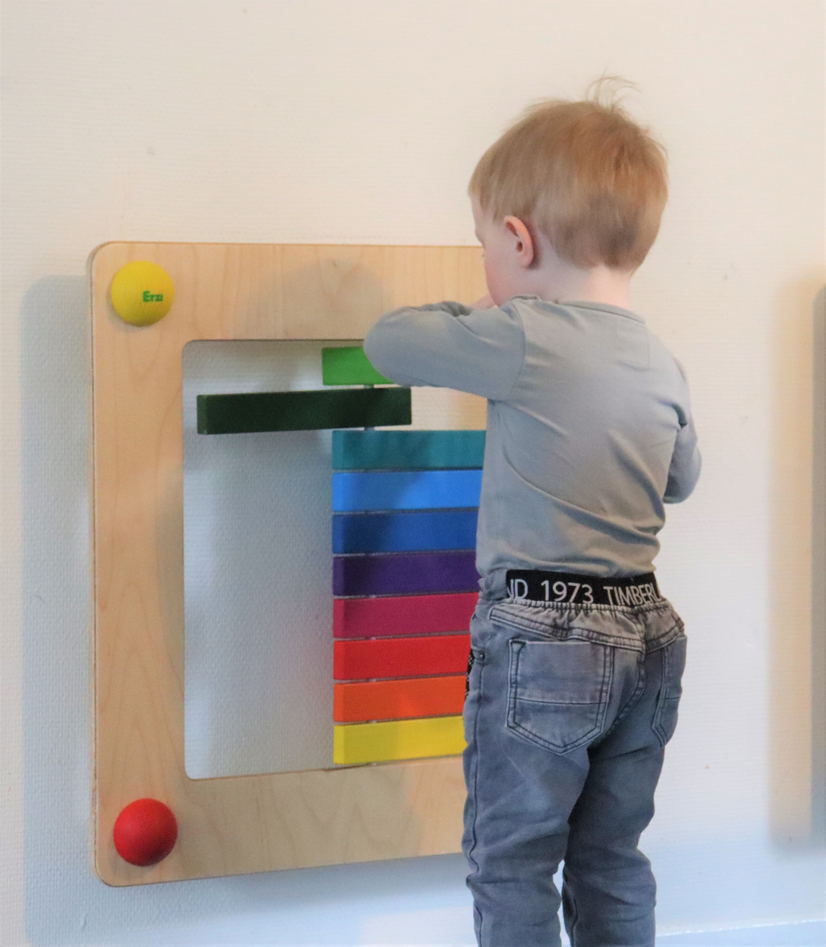 Dagplejebarn leger med aktivitetsmøbel på væggen
